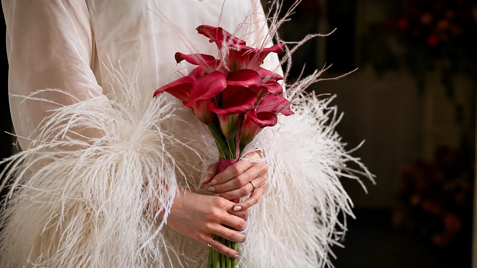 Bride holding a dramatic bouquet of dark red calla lilies paired with soft decorative grasses for a contemporary wedding look