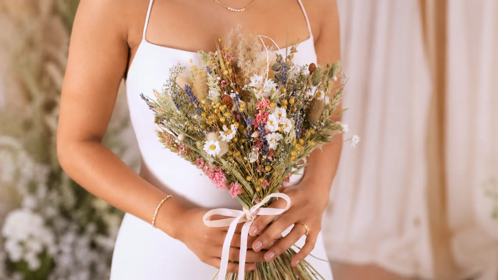Bride holding a boho dried wildflower wedding bouquets tied with a white ribbon