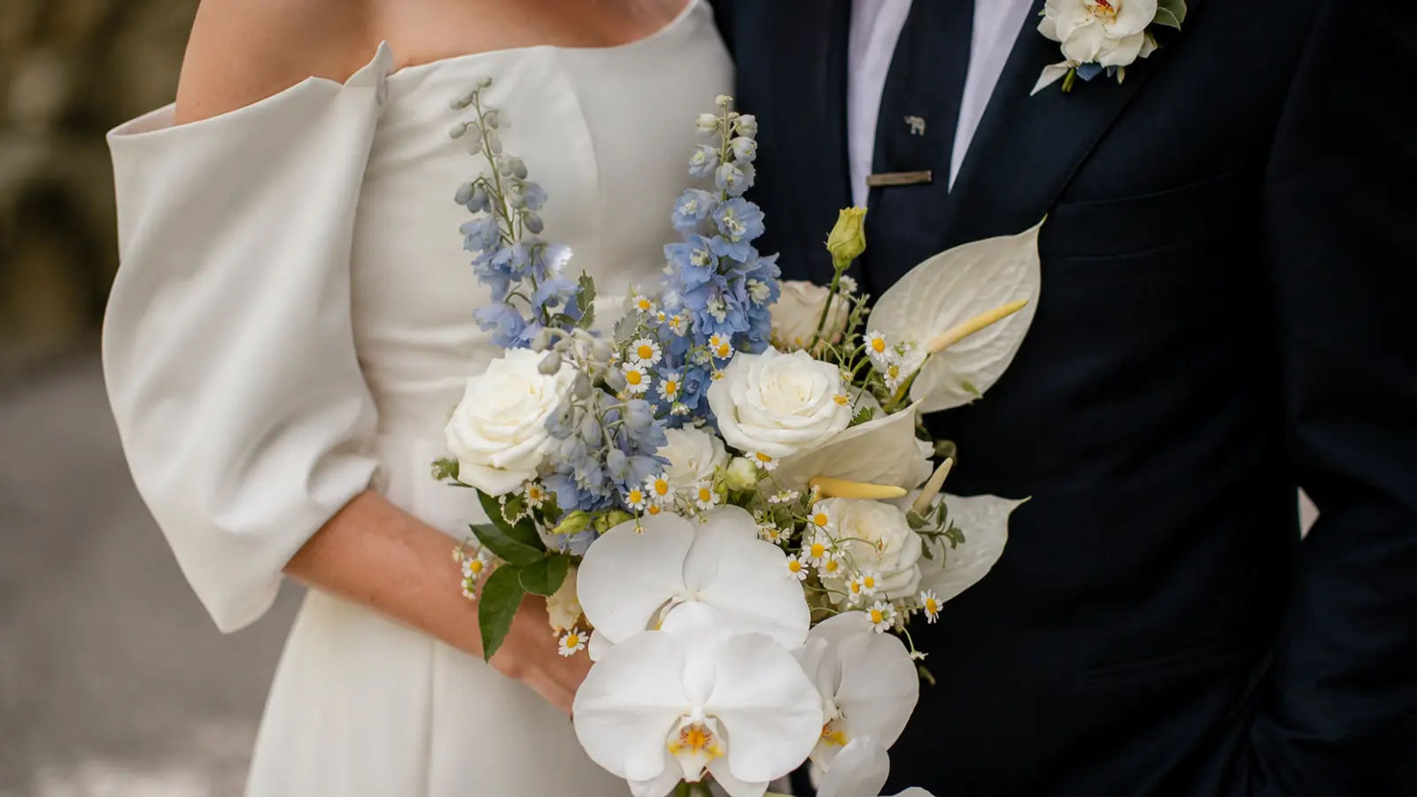 Bride holding a dusty blue and white wedding bouquet with orchids, roses and delphinium Blue Wedding Bouquets