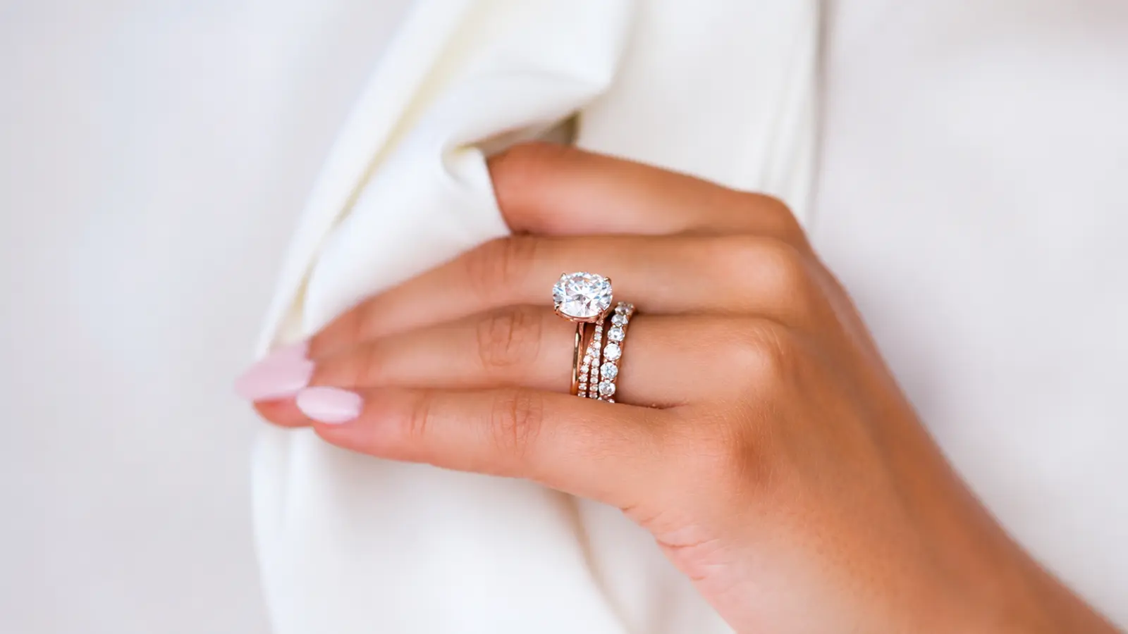 Woman wearing elegant stackable wedding rings with a solitaire engagement ring and matching diamond bands, creating a refined layered bridal jewelry look with timeless appeal