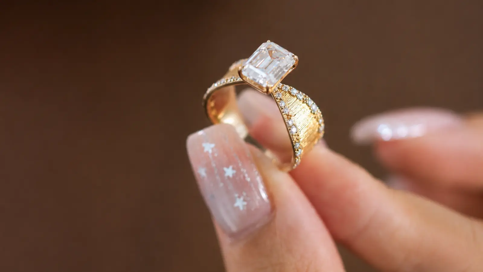A close-up of an Art Deco emerald cut engagement ring with engraved yellow gold shoulders and shimmering accent diamonds