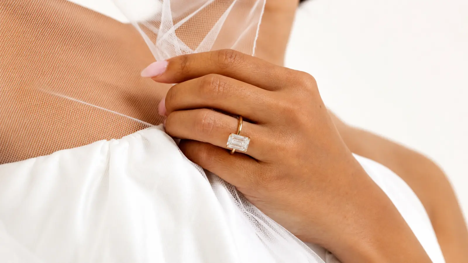 A bride gently holds her veil while wearing an emerald cut engagement ring in a classic yellow gold solitaire setting Emerald Wedding Rings