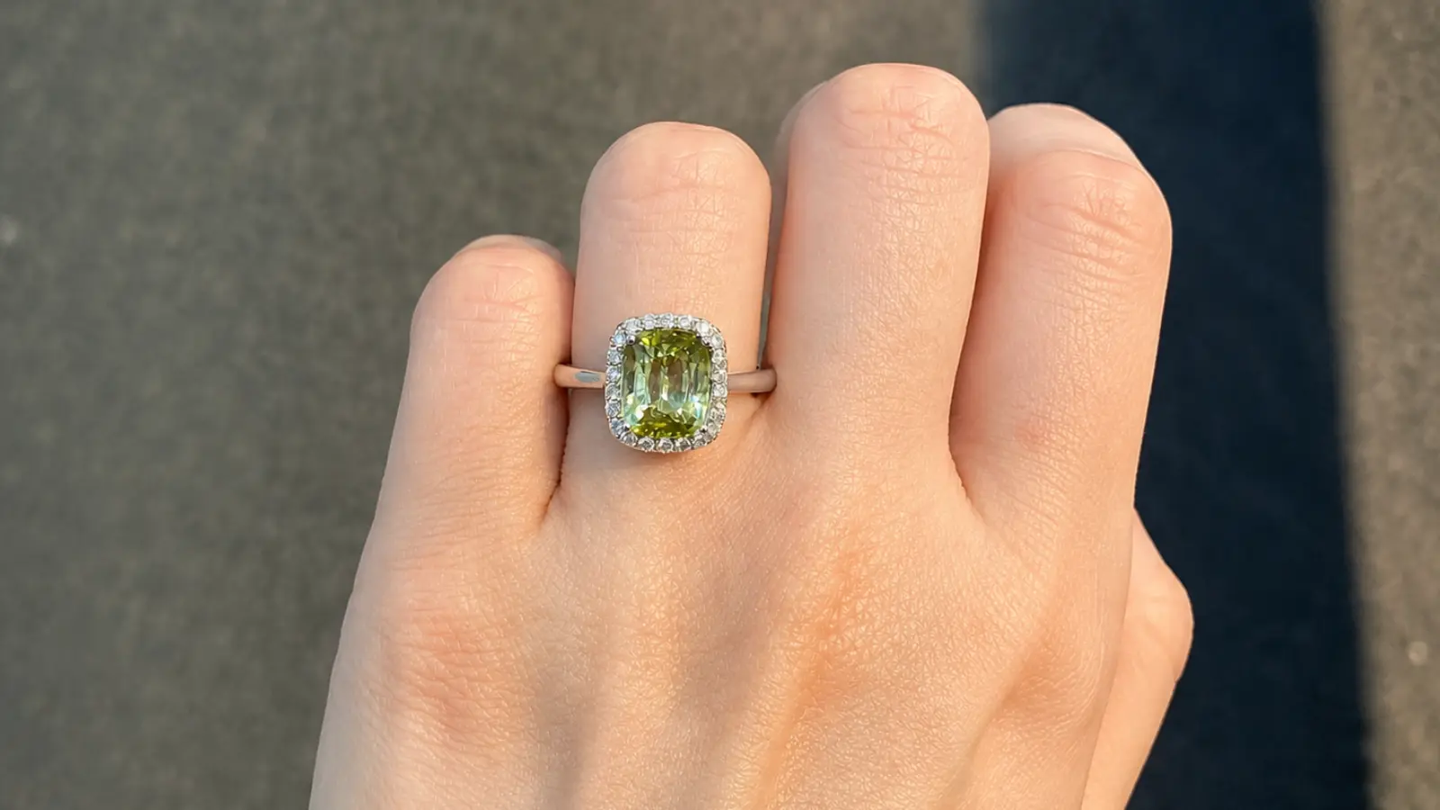 A hand wears an emerald halo engagement ring with a cushion-cut green center stone framed by brilliant diamonds in a white gold setting