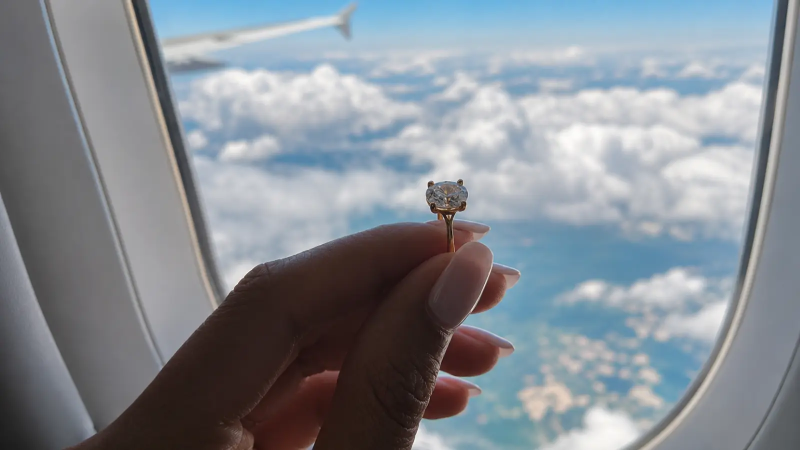 An engagement ring held near an airplane window while traveling by air