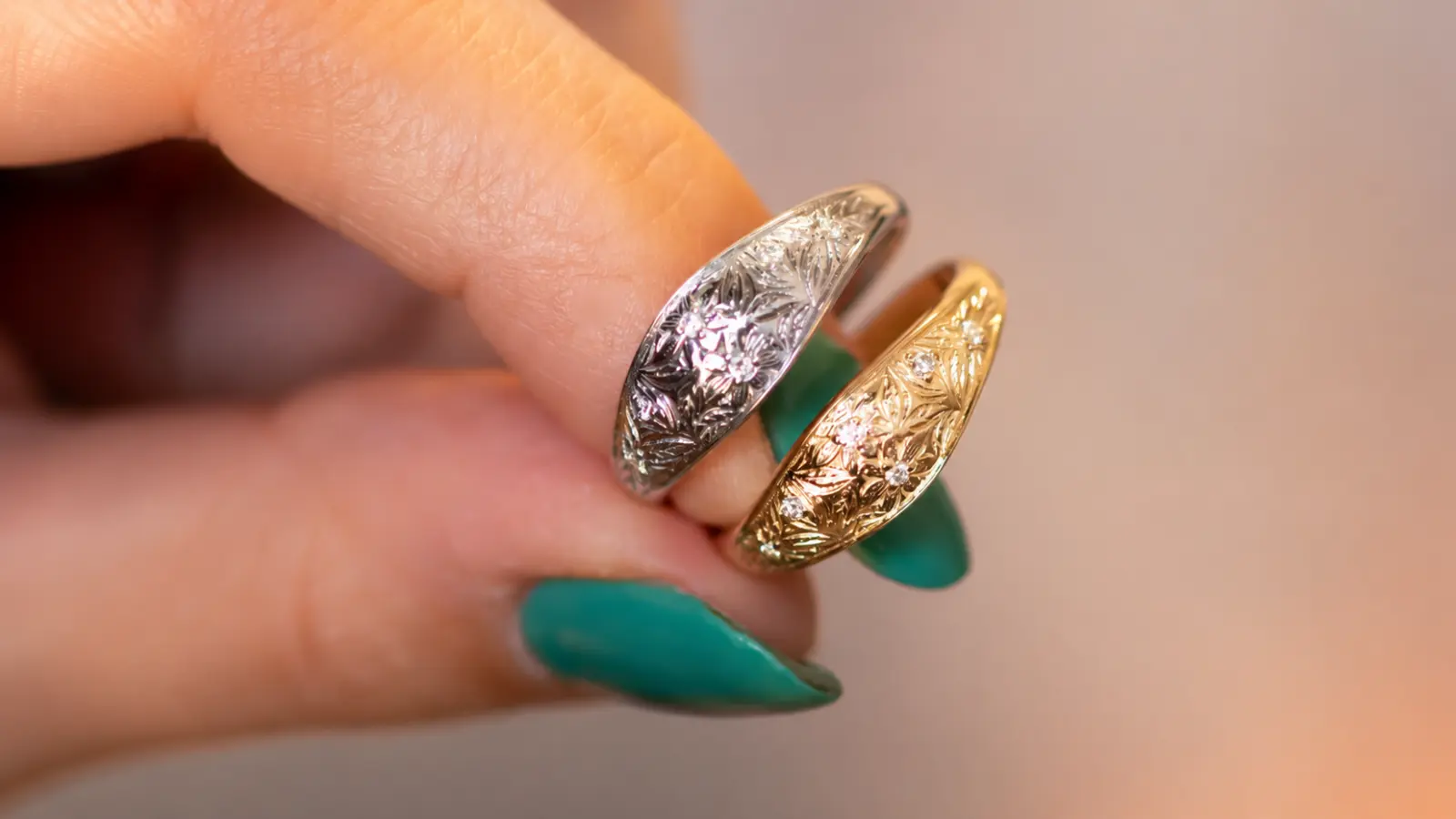 Two engraved floral wedding bands with botanical patterns and small diamond accents displayed side by side