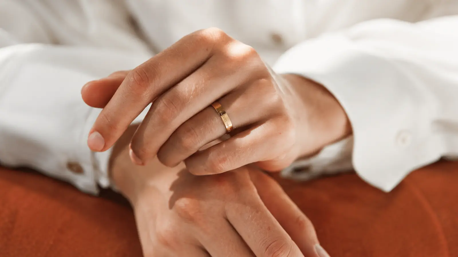 A hand wearing an engraved minimalist gold wedding band with a sleek polished finish and understated contemporary styling