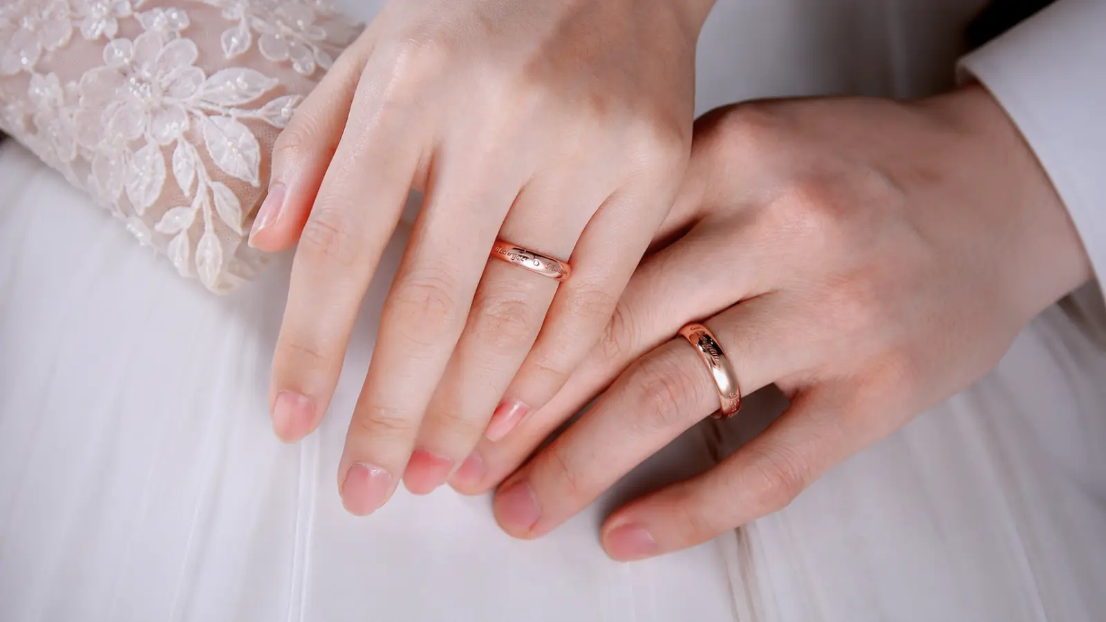 A bride and groom rest their hands together while wearing engraved rose gold wedding rings, showcasing personalized details, polished finishes and the signature warm blush color of rose gold wedding bands