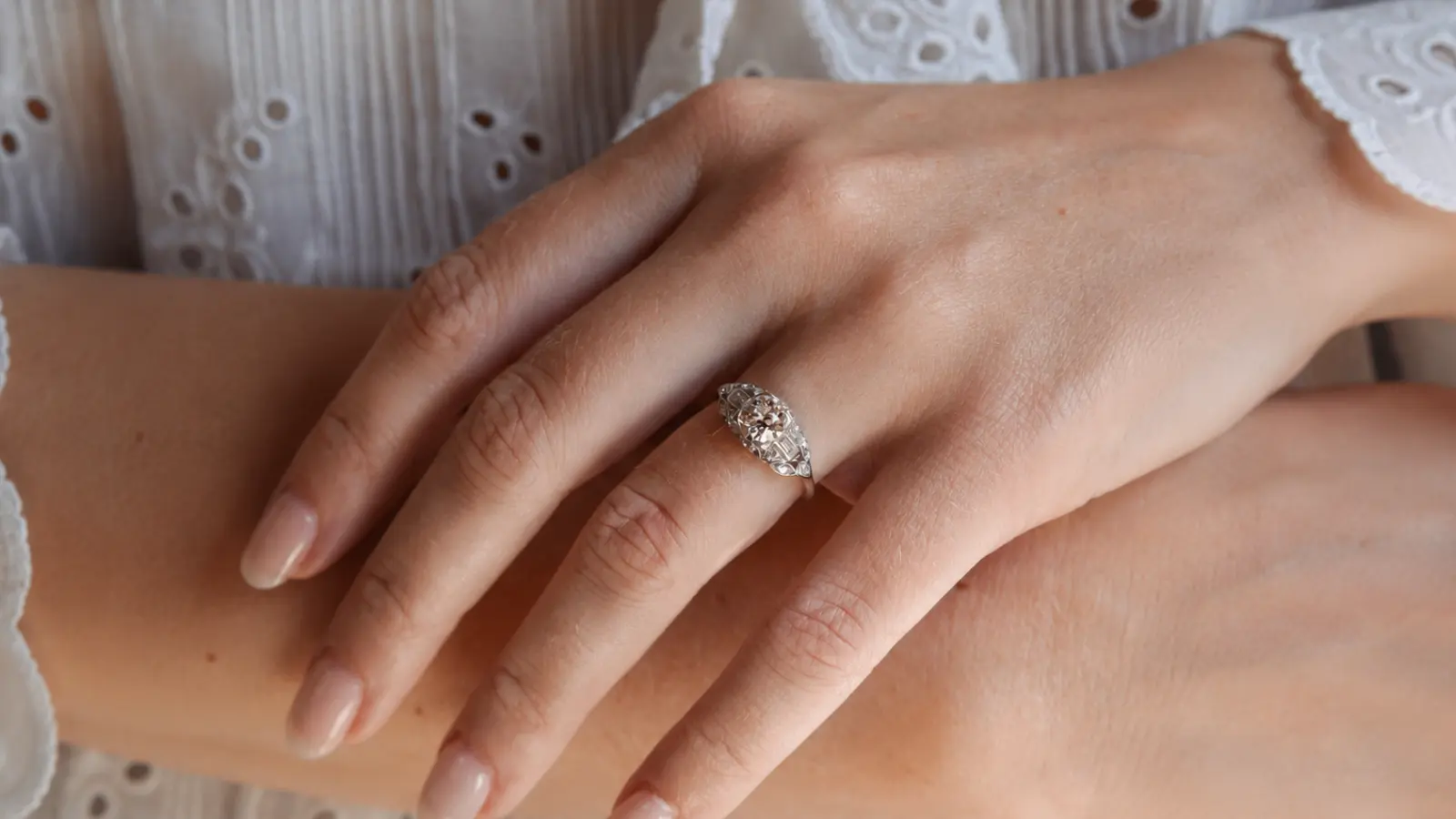A hand displaying a filigree Art Deco marquise diamond ring with intricate openwork details and an elongated antique-inspired design