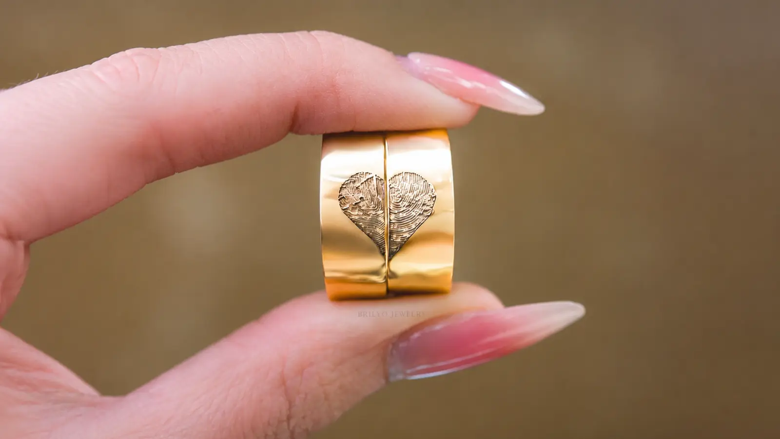 Two custom gold wedding rings with a shared fingerprint engraving forming a heart when placed together