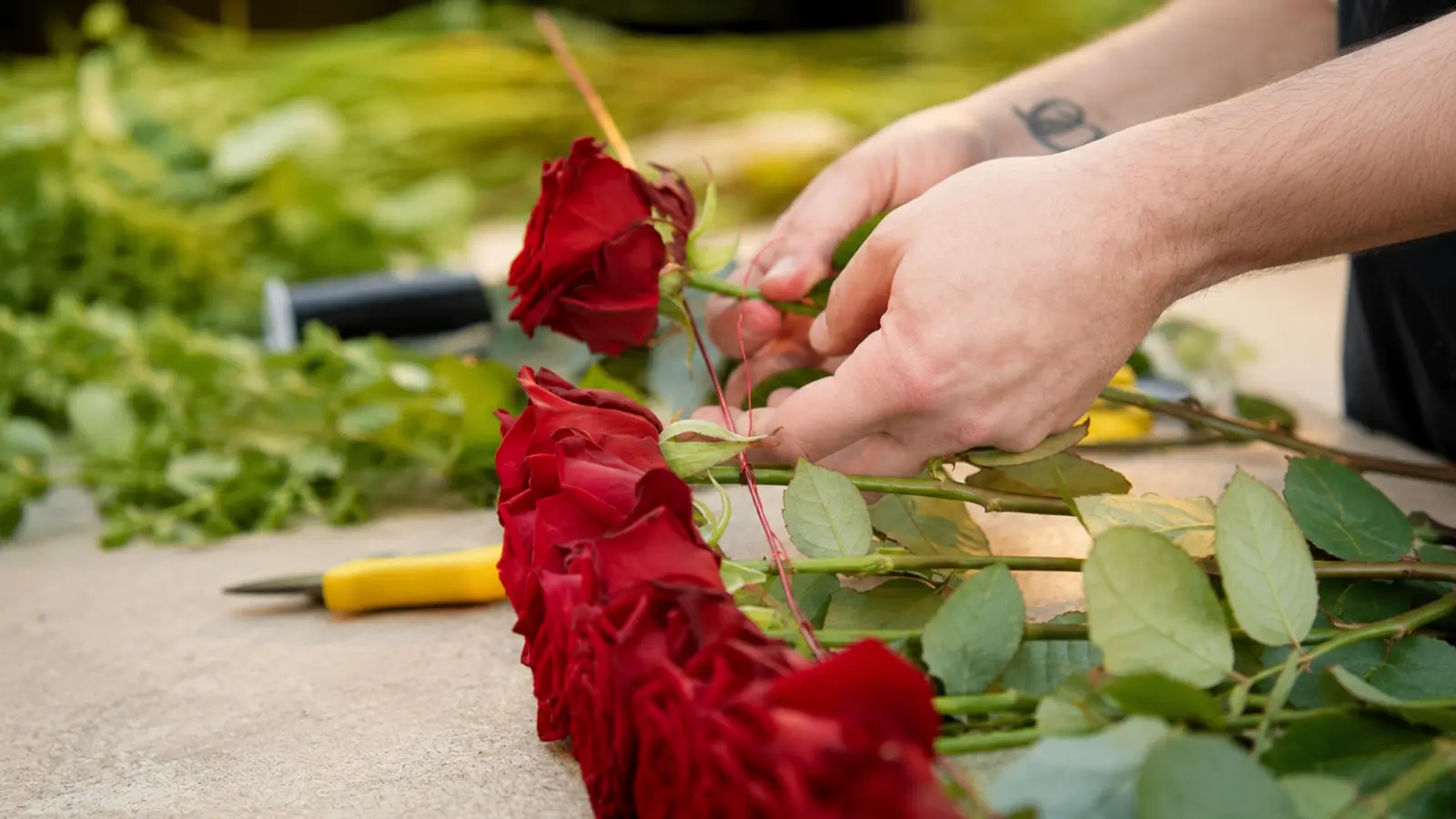Close-up of a florist binding fresh red roses together to create a romantic wedding bouquet