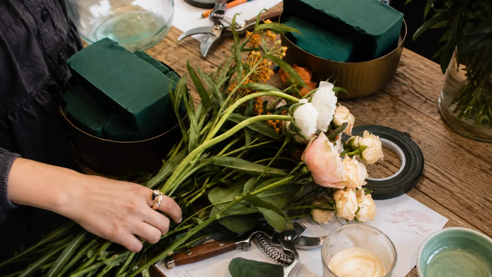 Florist preparing fresh pink flowers and bouquet supplies on a wooden worktable before arranging a wedding bouquet