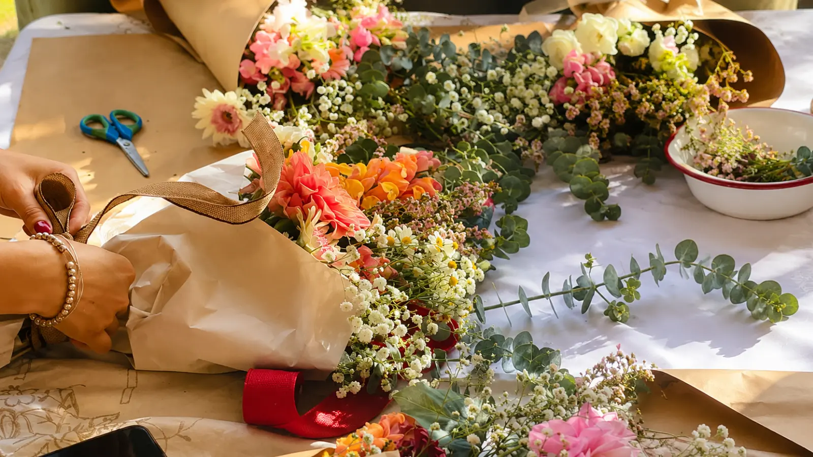 Florist wrapping a colorful wedding bouquet with kraft paper, eucalyptus and fresh seasonal flowers