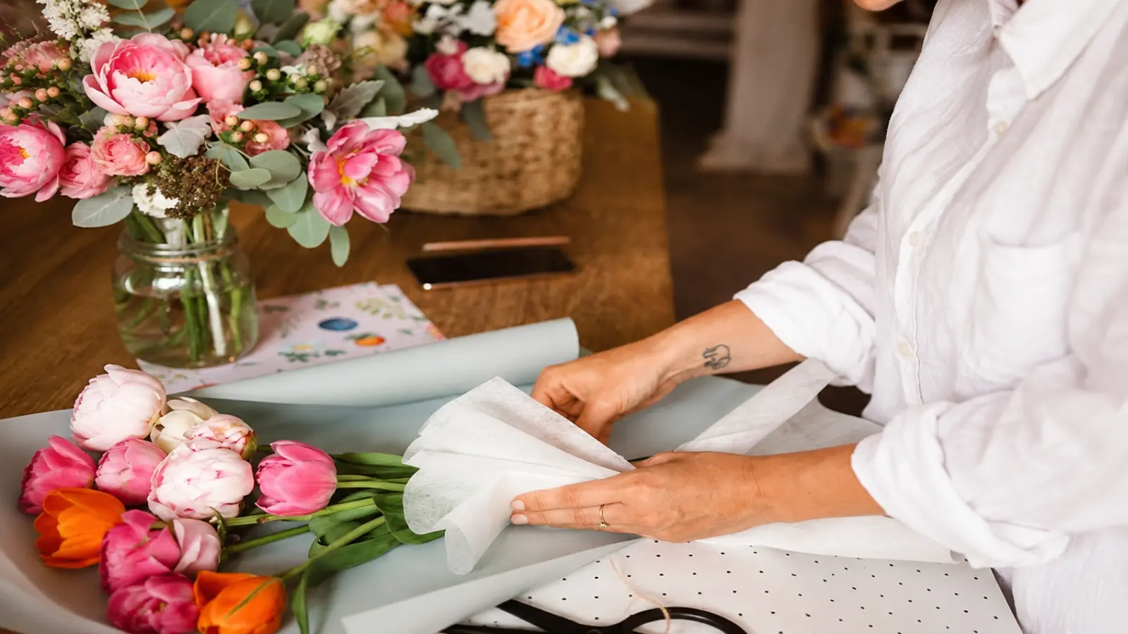 Florist wrapping a fresh wedding bouquet with tulips, peonies and eucalyptus