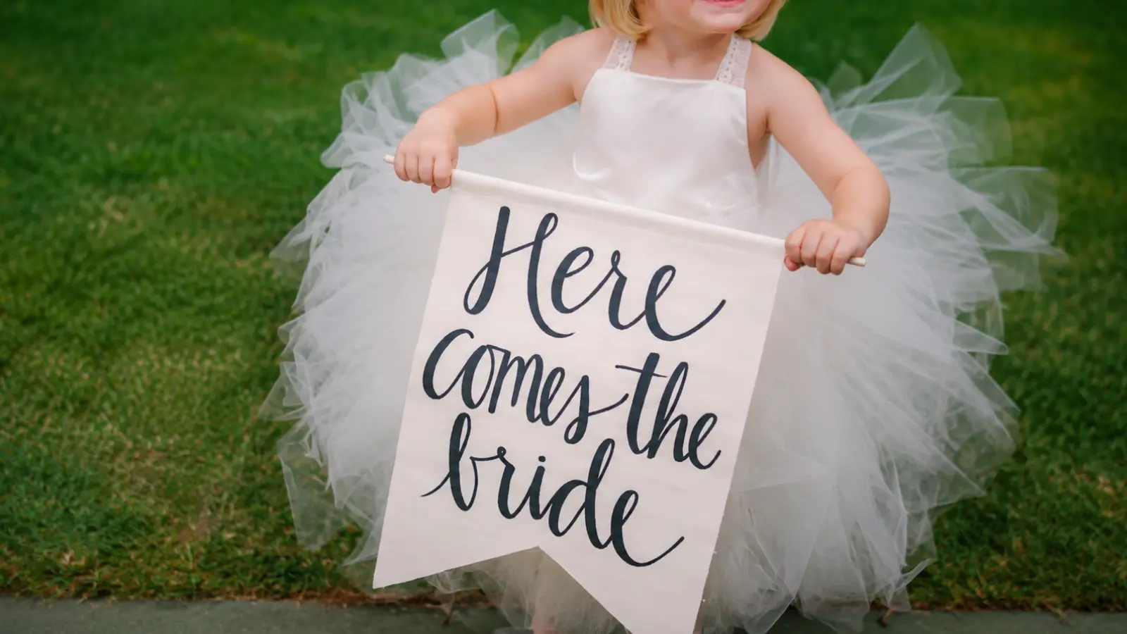 Flower girl carrying a Here Comes the Bride sign instead of flowers