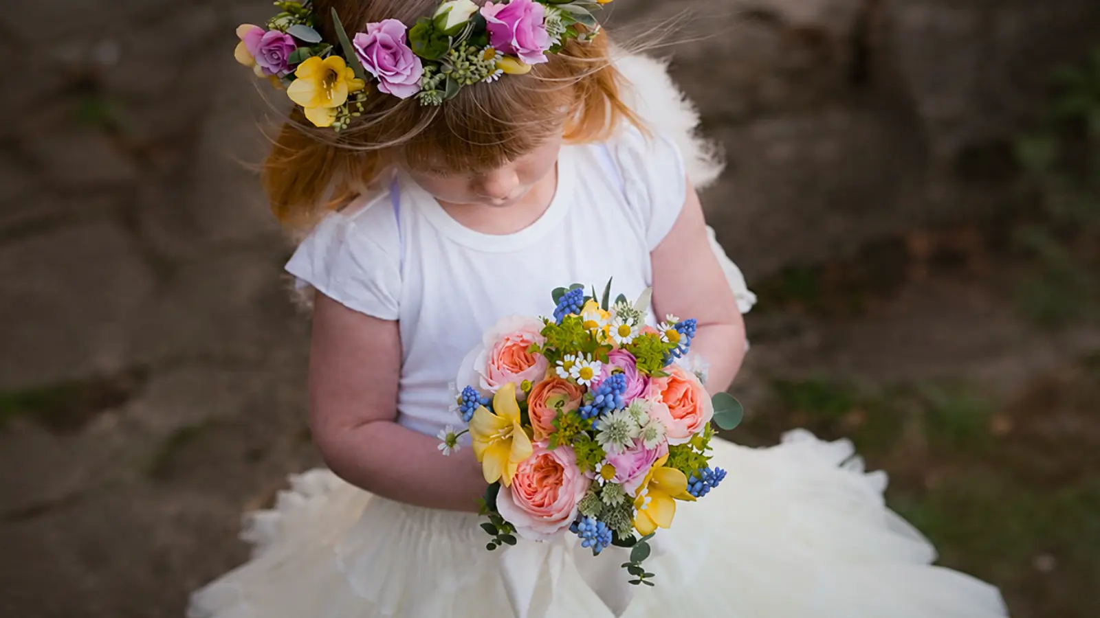 Flower girl holding a mini wedding bouquet while wearing a colorful floral crown