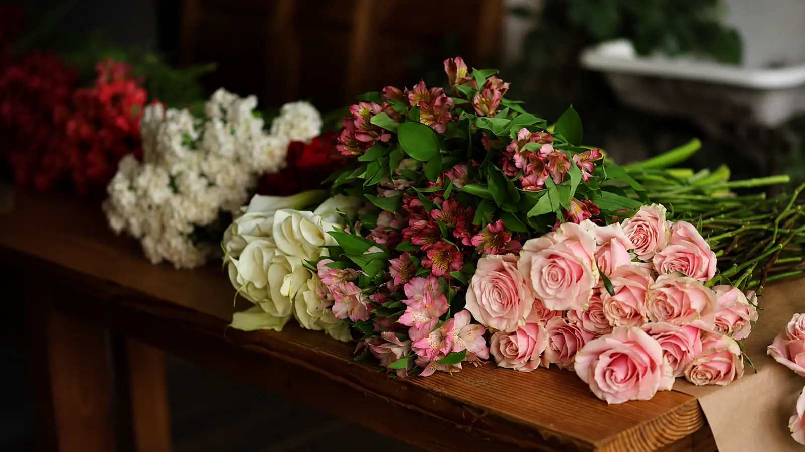 Pink roses, white roses, alstroemeria, and other fresh flowers arranged on a table before assembling a wedding bouquet