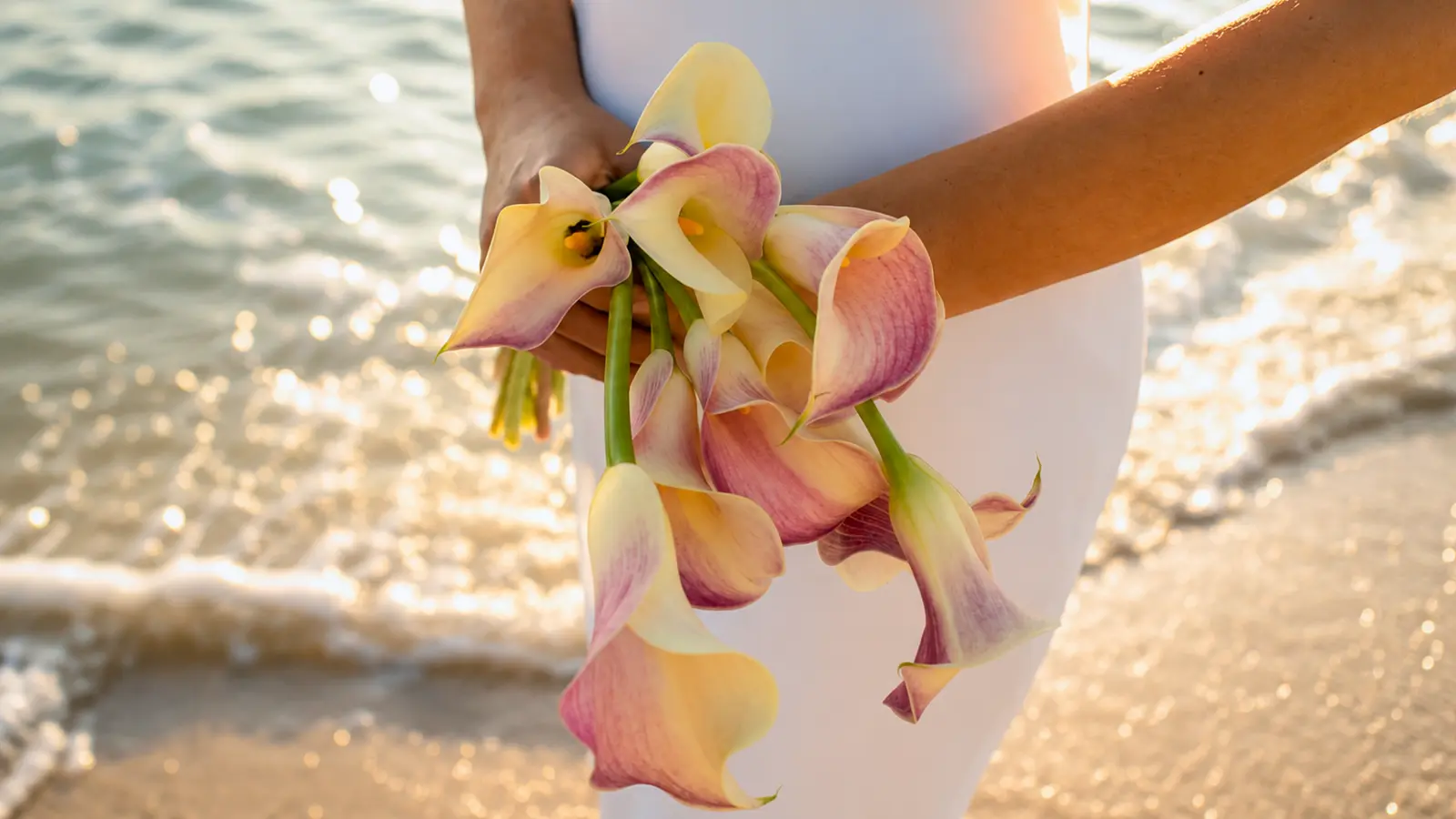 Bride holding a fresh pink calla lily wedding bouquet on a beach