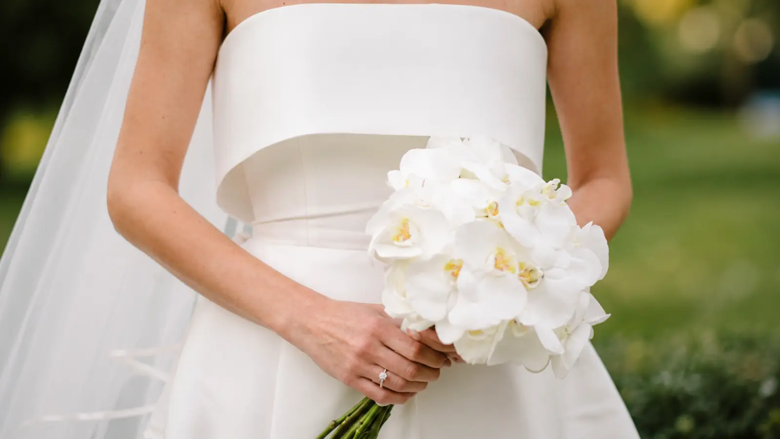 Bride holding a fresh white orchid wedding bouquet with cascading natural stems Fresh vs. Artificial Wedding Bouquets