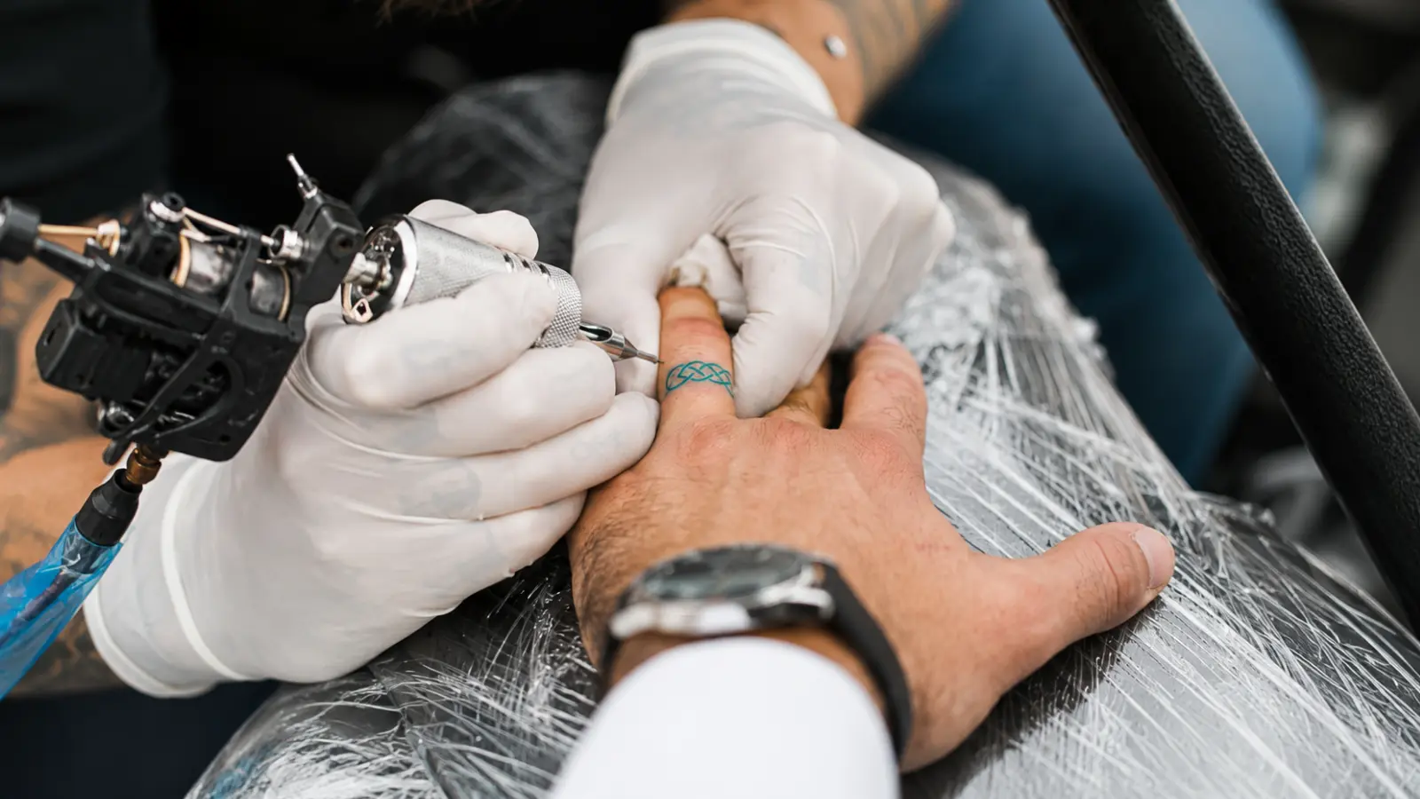 A tattoo artist applying a wedding ring tattoo on a client's ring finger