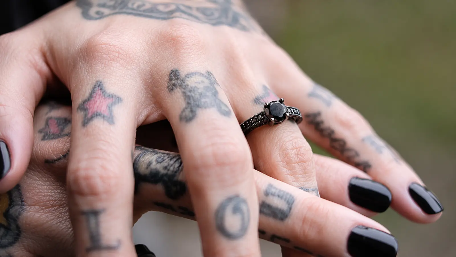 A tattooed hand wearing a gothic black diamond engagement ring with a dark pavé band and round black center stone Gothic Wedding Rings
