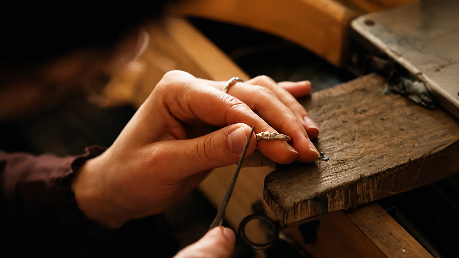 A jewelry artisan carefully handcrafting a custom wedding ring at a traditional jeweler's bench using precision hand tools