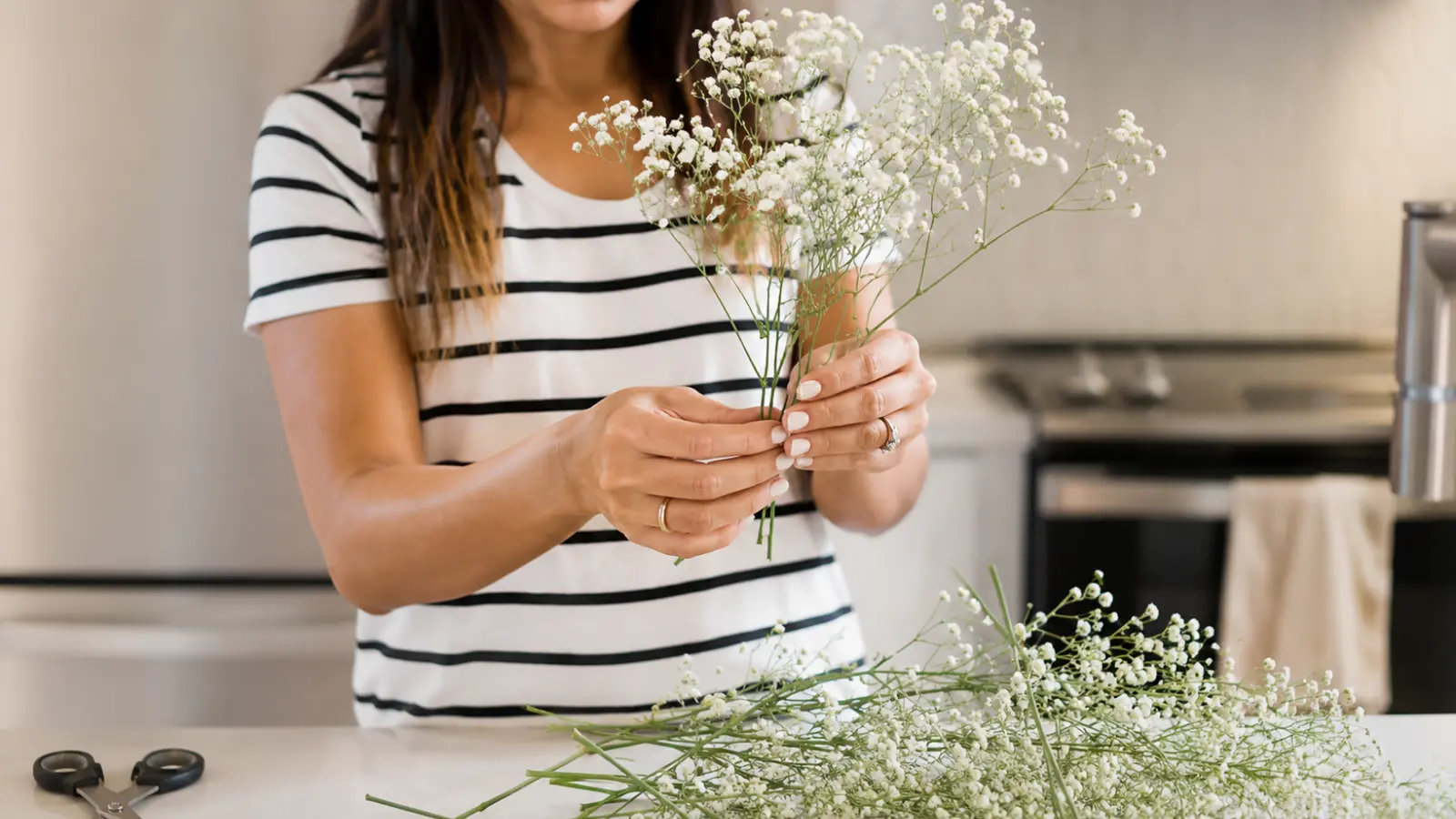 Woman arranging fresh baby's breath flowers while creating a wedding bouquet at home