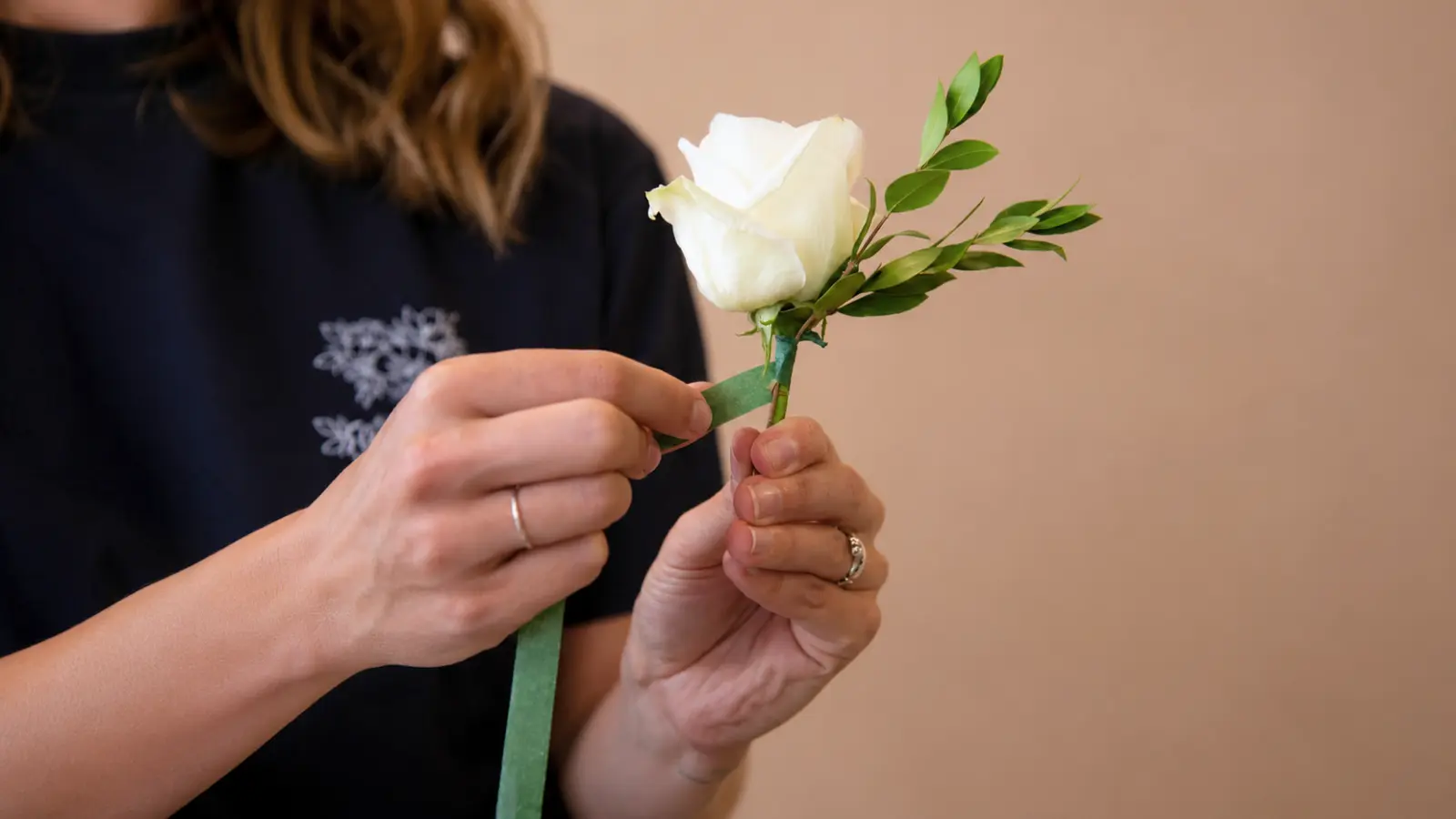 Florist wrapping a white rose wedding boutonniere with green floral tape