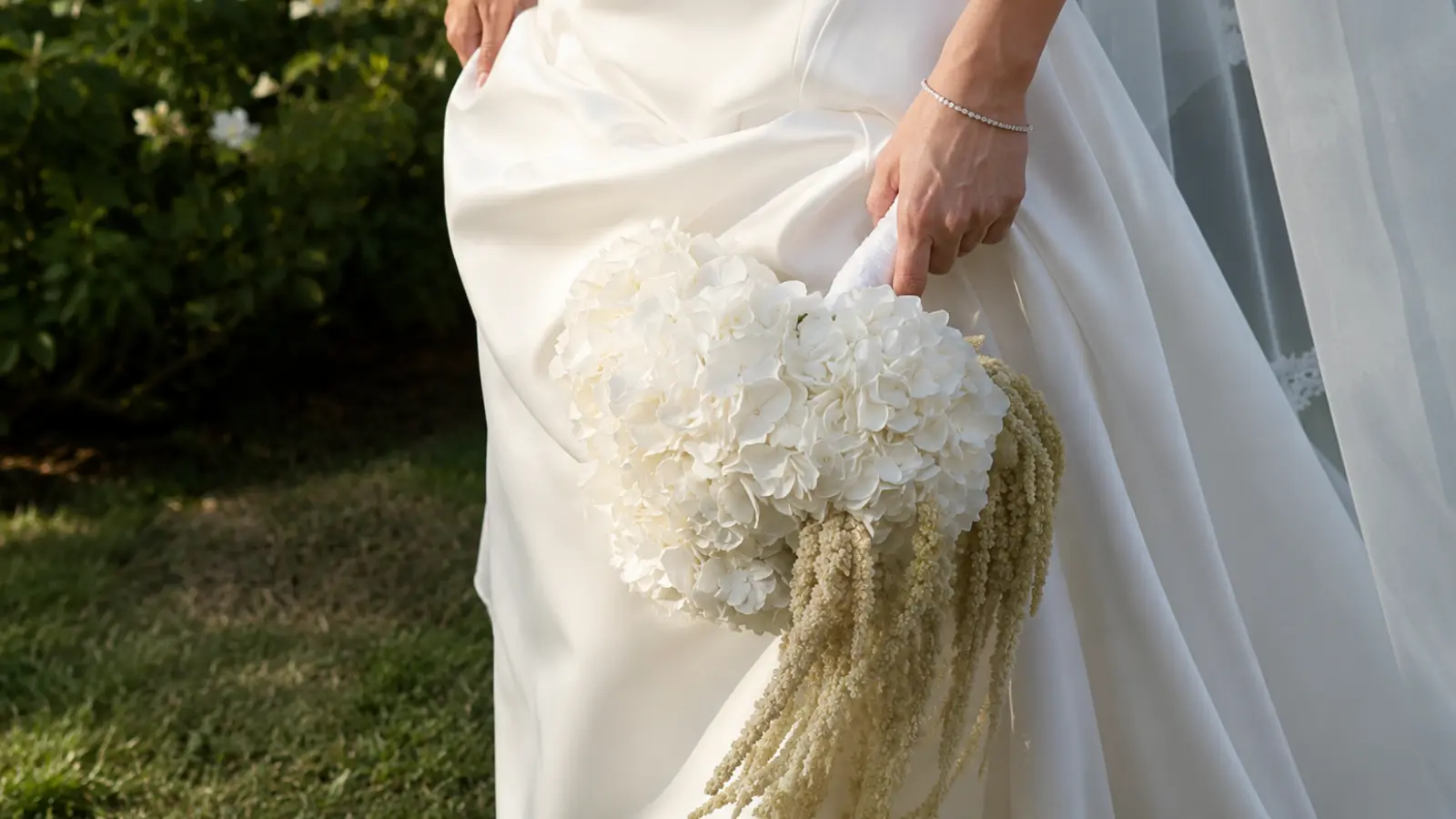 Bride carrying a cascading white hydrangea wedding bouquet with trailing hanging amaranthus