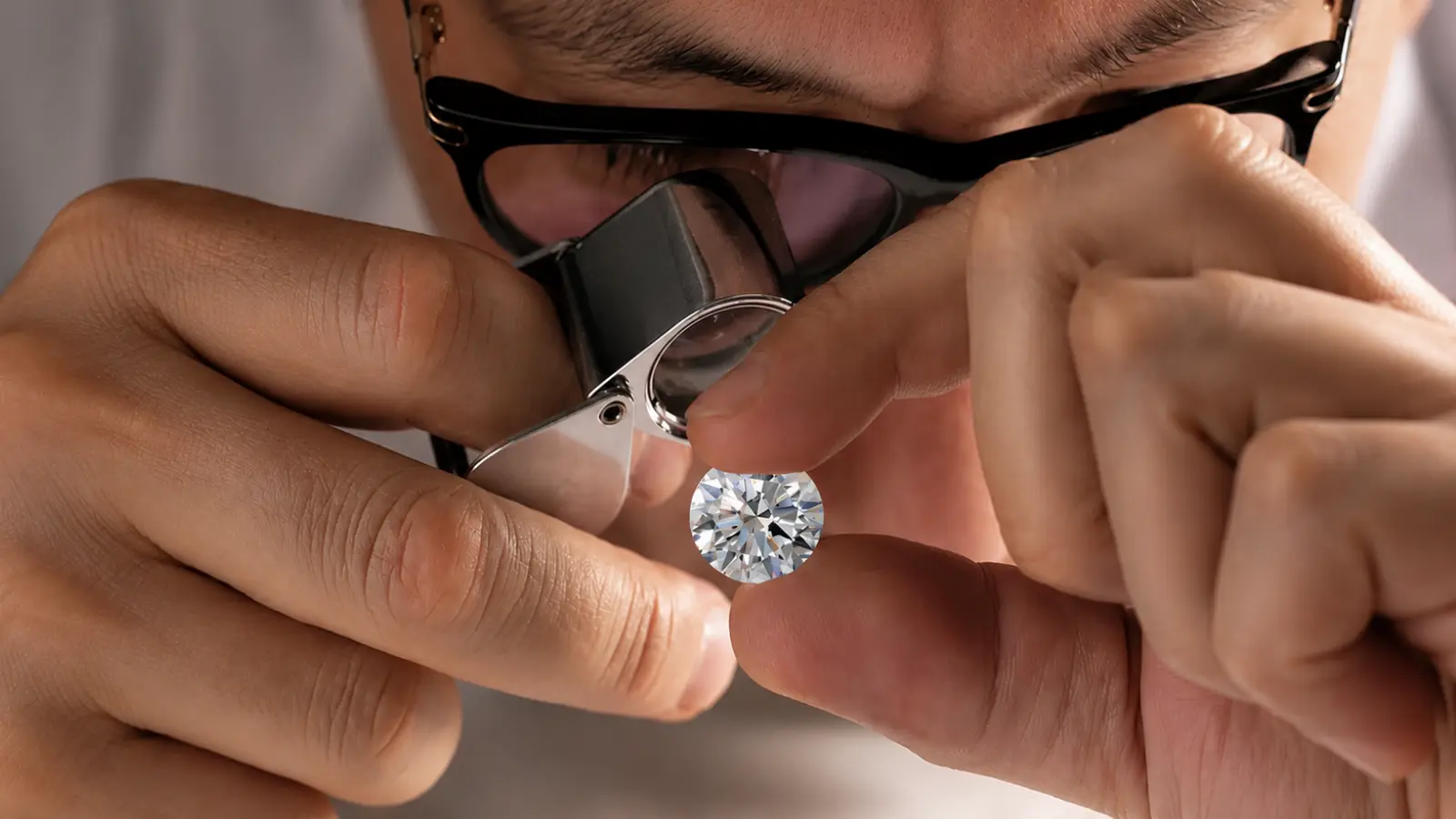 A gemologist examines a lab-grown diamond through a jeweler's loupe while holding the stone between precise fingertips during inspection