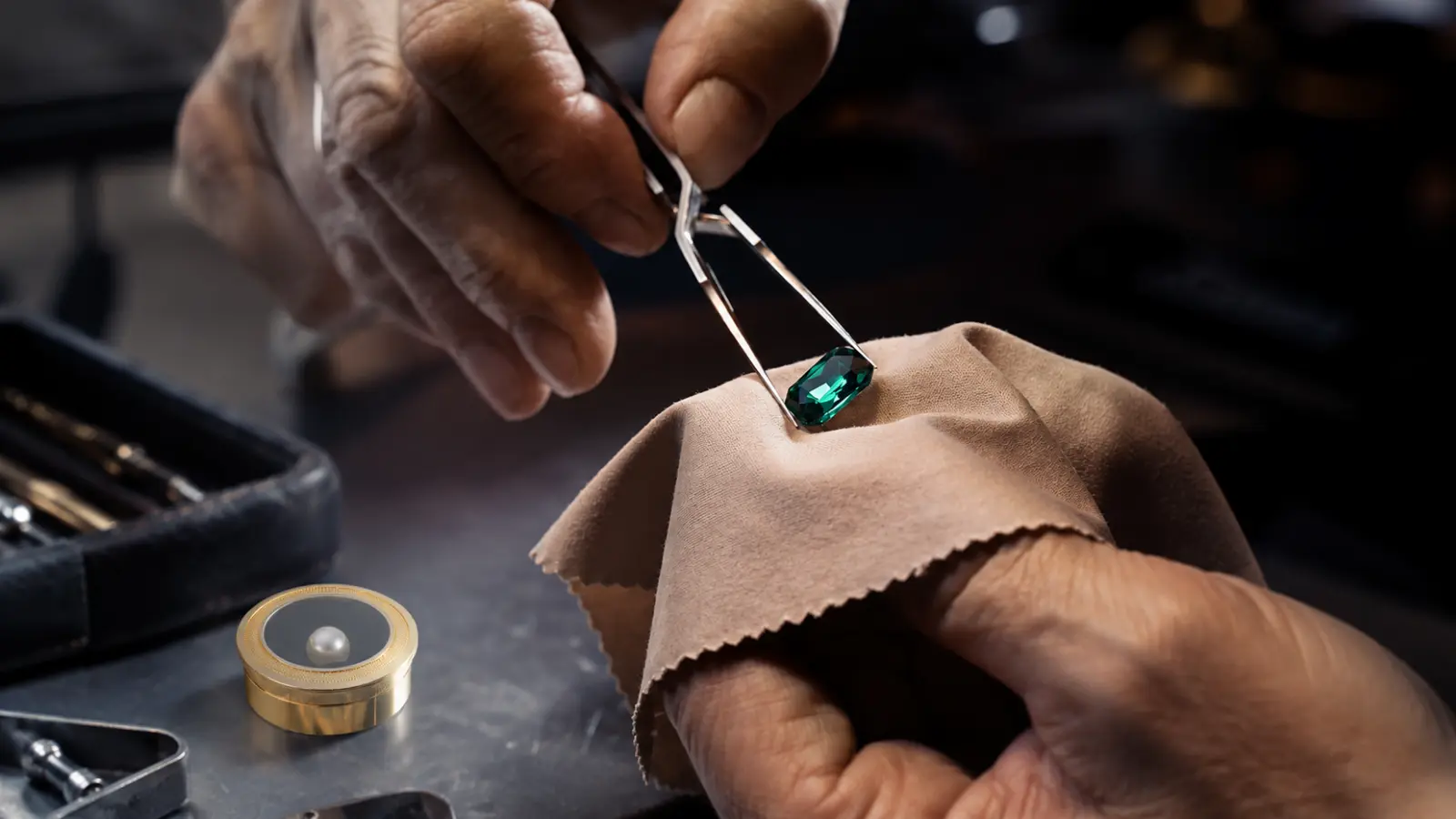 A jeweler holds a natural emerald gemstone with tweezers while inspecting its quality over a soft polishing cloth