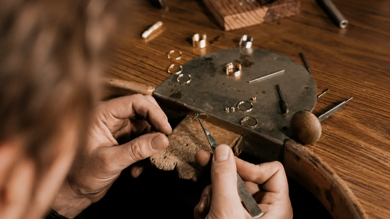 A jeweler inspecting and repairing a wedding ring at a traditional jewelry workbench with professional tools