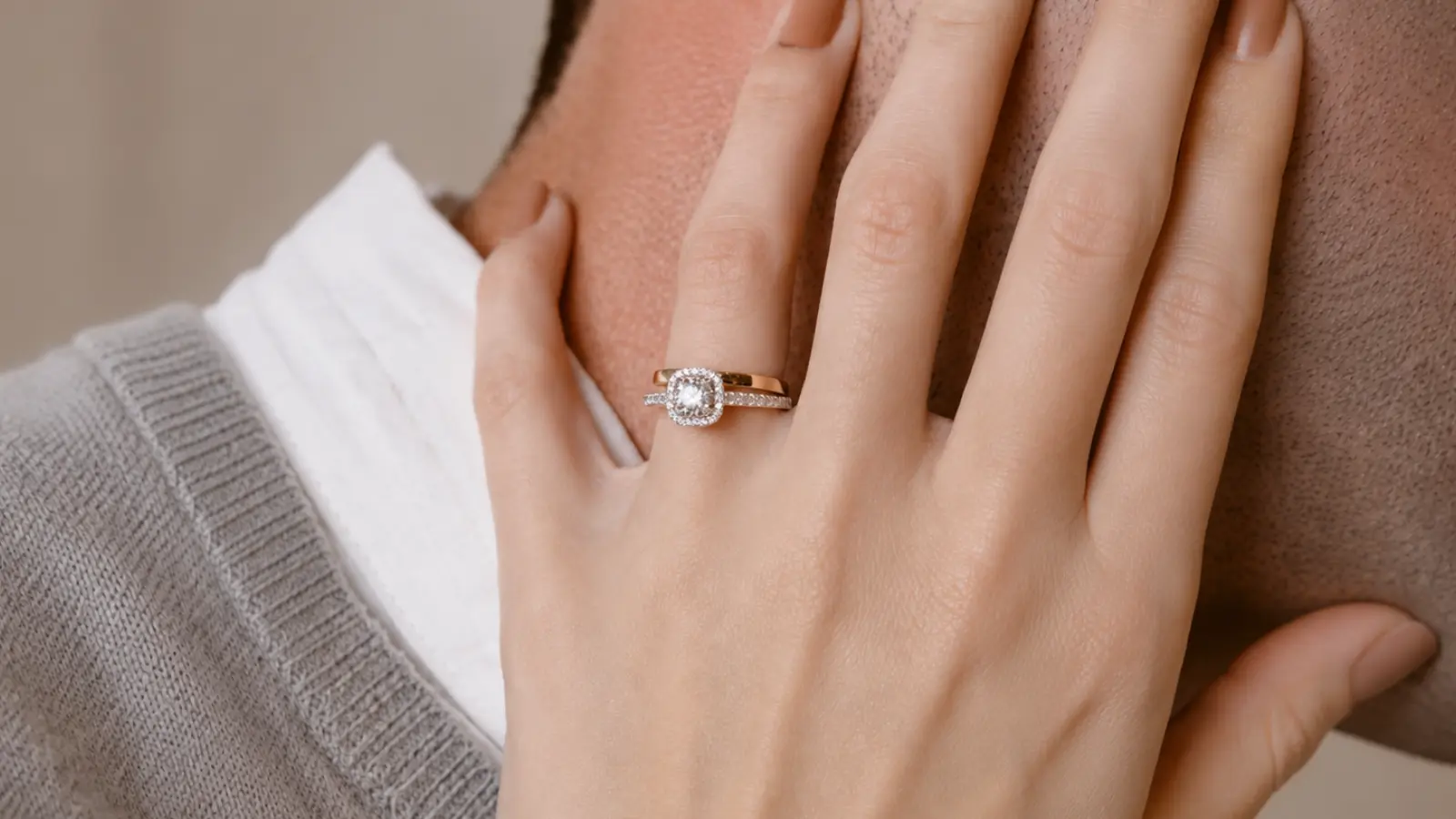 A hand rests on a partner's shoulder while wearing a lab-grown diamond engagement ring with a halo setting and matching diamond wedding band