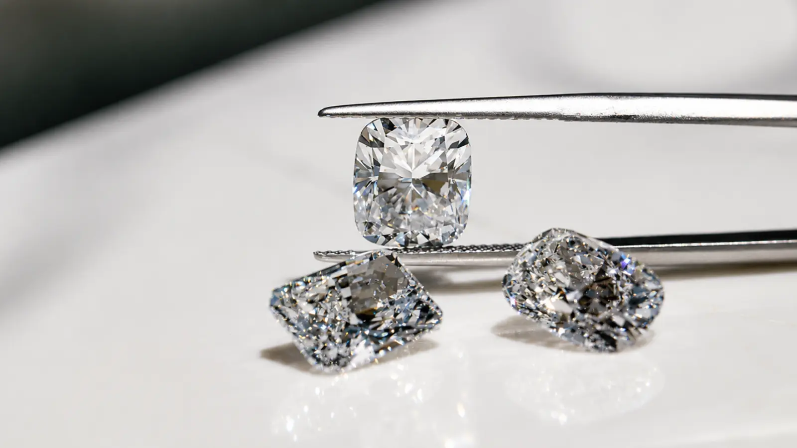 Several loose moissanite gemstones in cushion and radiant cuts are displayed beside precision tweezers under bright natural lighting