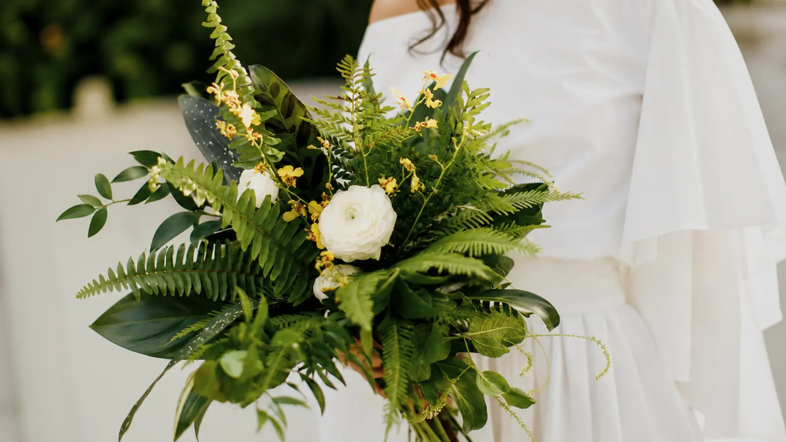 Bride holding a lush greenery wedding bouquet with tropical foliage ferns and elegant white flowers