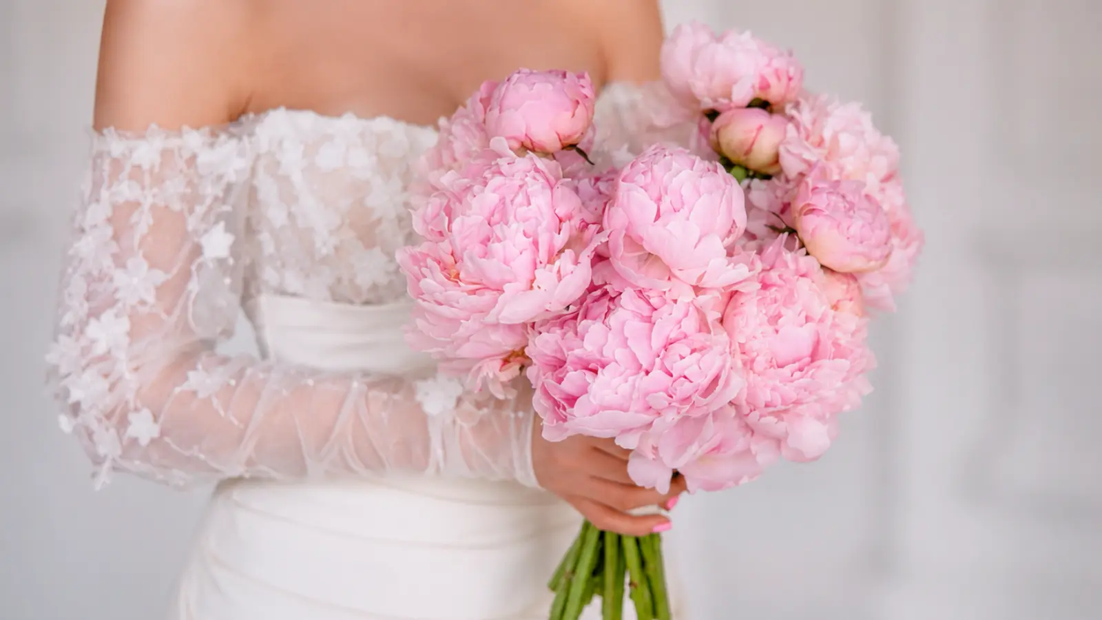 Bride wearing a lace wedding dress while holding a lush round bouquet of light pink peonies