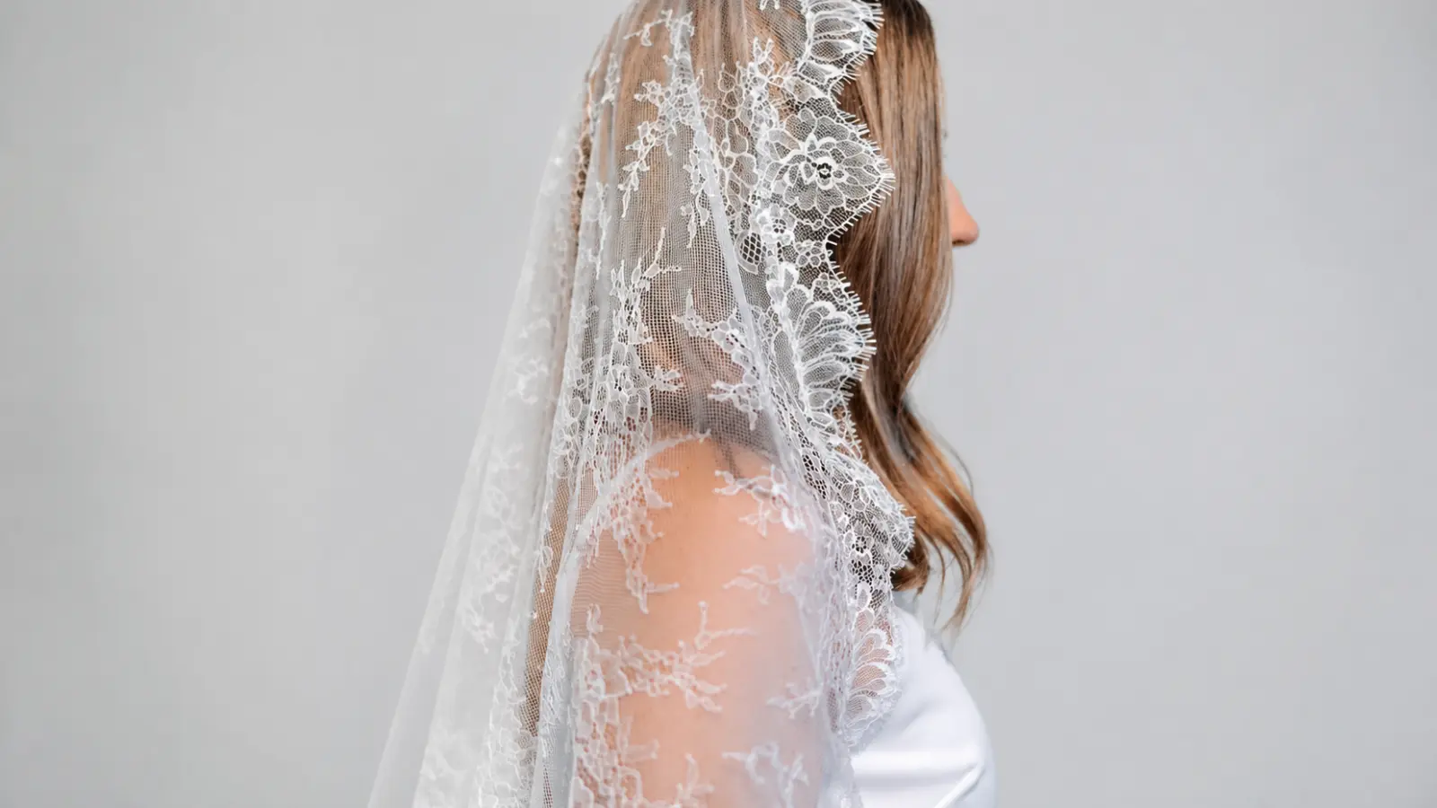 Rear view of a bride wearing a mantilla wedding veil with ornate lace extending down the back