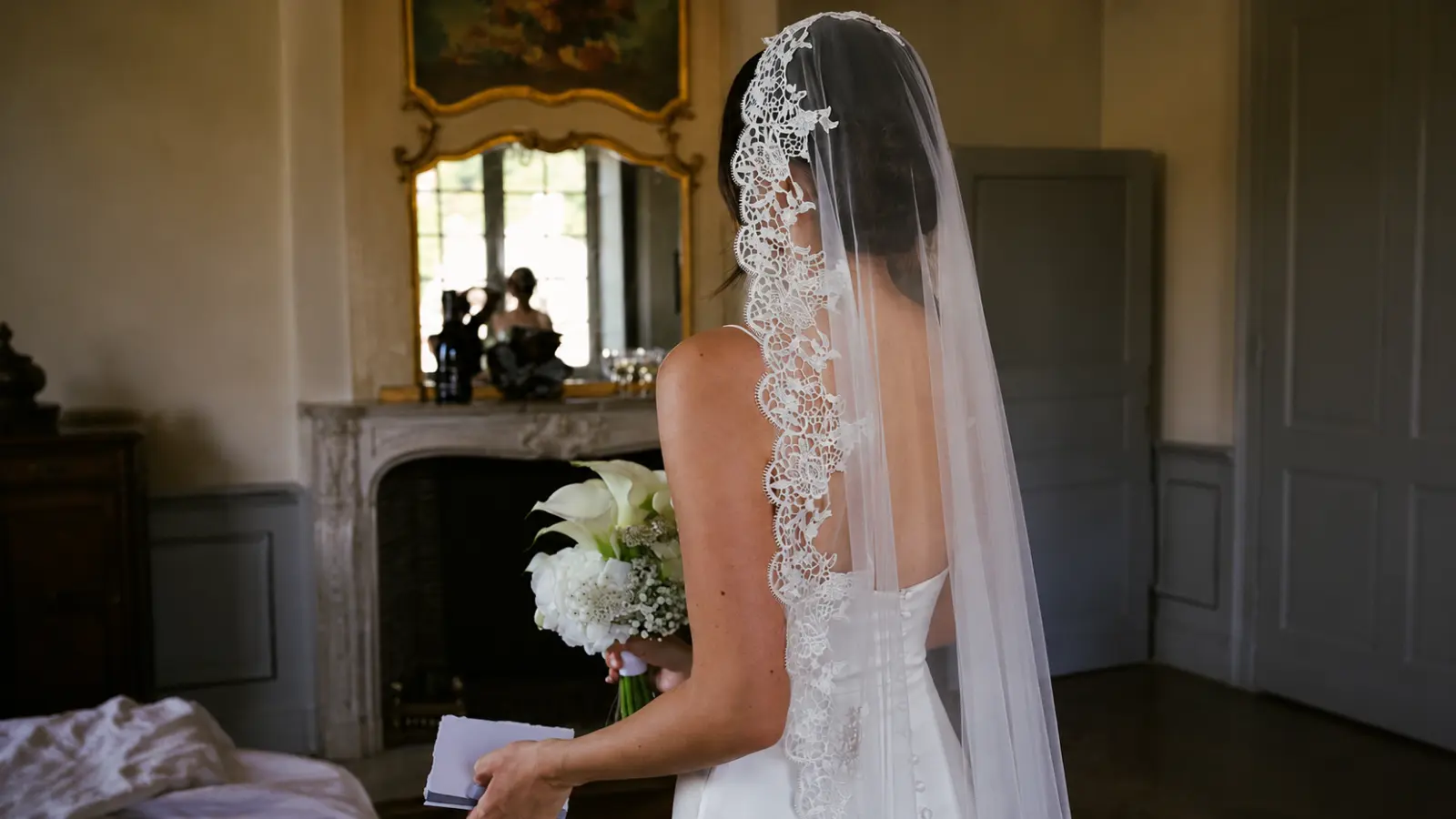 Side profile of a bride wearing a mantilla wedding veil with floral lace framing the face