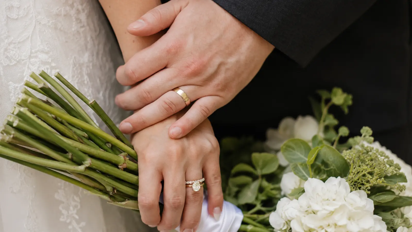 Bride and groom wearing matching gold wedding rings while holding a white wedding bouquet Wedding Ring Sets