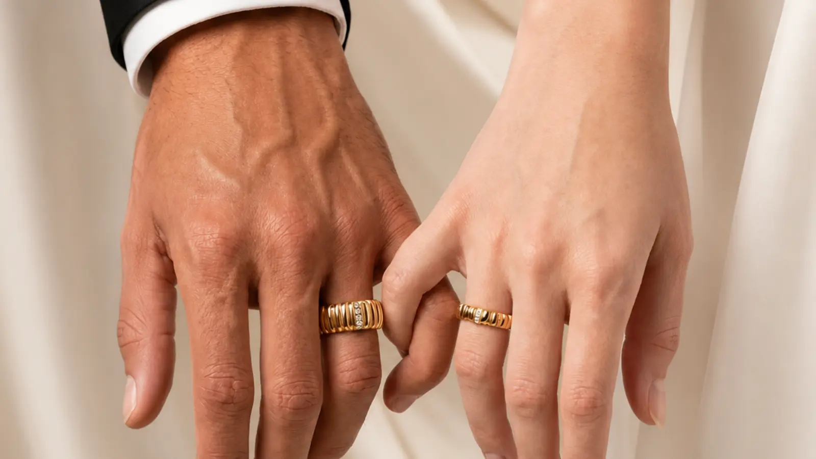 A couple wears coordinated textured gold wedding bands with complementary engraved details, showing how matching rings can share a common design without being identical