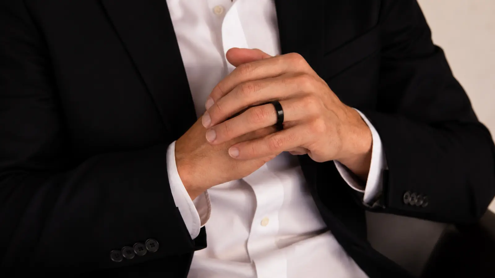 A man wearing a matte black men's wedding band with a tailored black suit and crisp white dress shirt