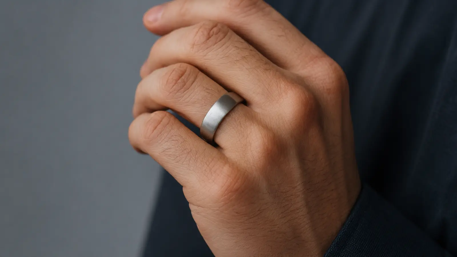A close-up of a hand wearing a matte titanium wedding ring, emphasizing its understated style, durable finish and lightweight construction