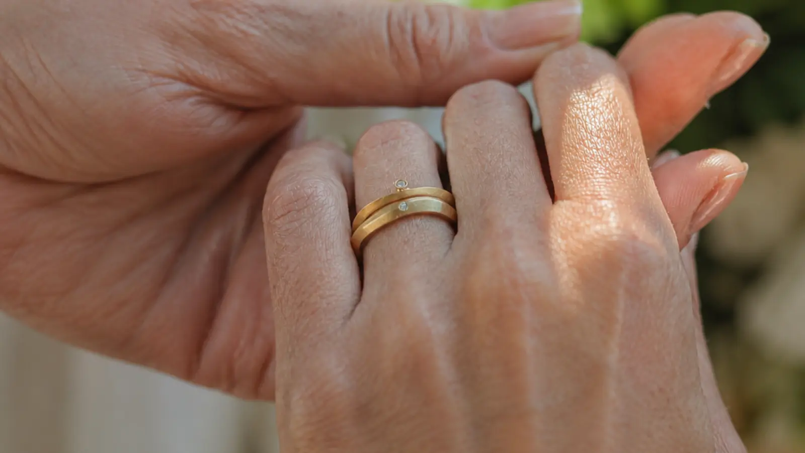 Two stacked matte yellow gold wedding rings with delicate diamond accents are worn together on one finger, illustrating a contemporary layered look that maintains the classic warmth of yellow gold