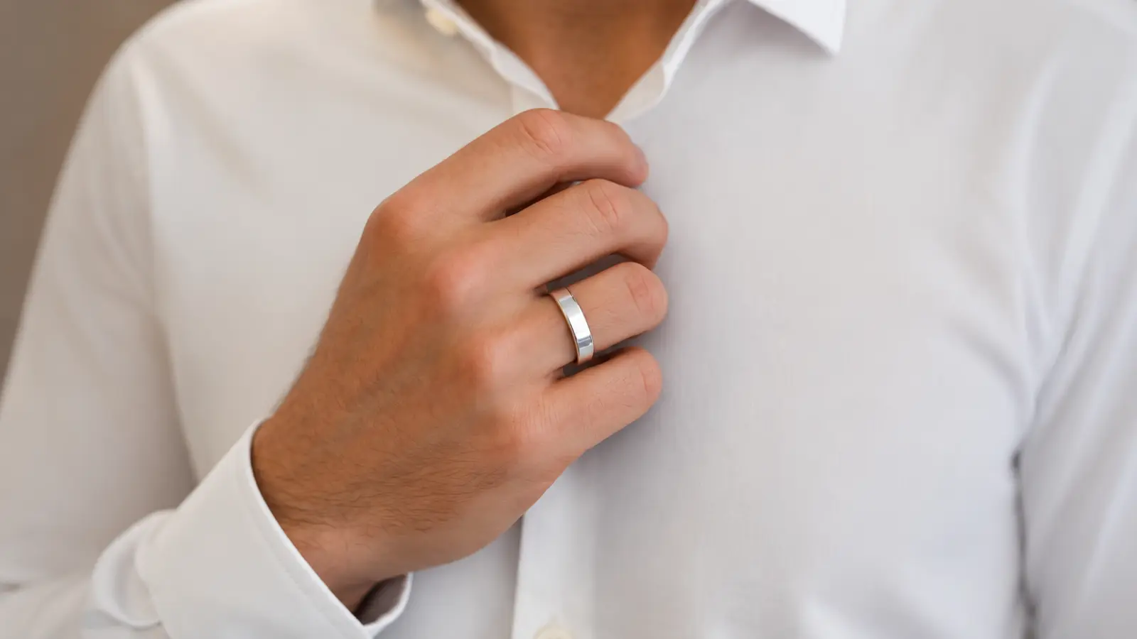 A man adjusts his shirt while wearing a polished platinum wedding ring, emphasizing the clean modern design, bright white metal and durable construction of a platinum band