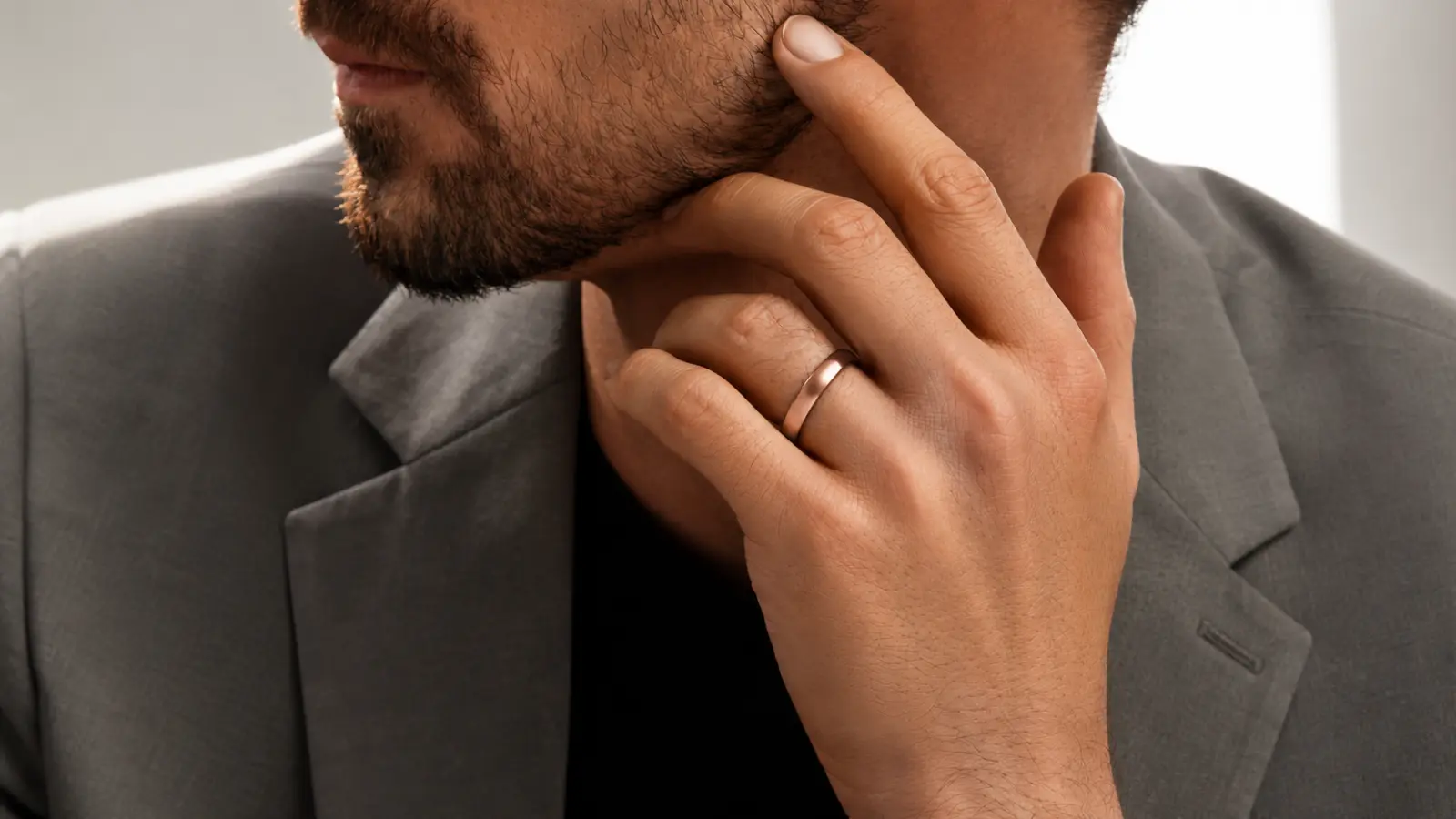 A groom touches his face while wearing a polished rose gold wedding ring, highlighting the sleek modern design and warm elegant color of a classic men's wedding band
