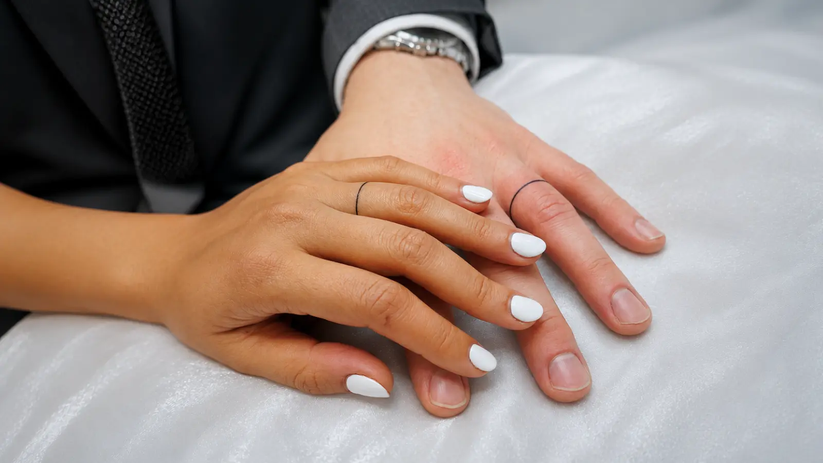 Minimalist black wedding ring tattoos on a couple's ring fingers representing marriage