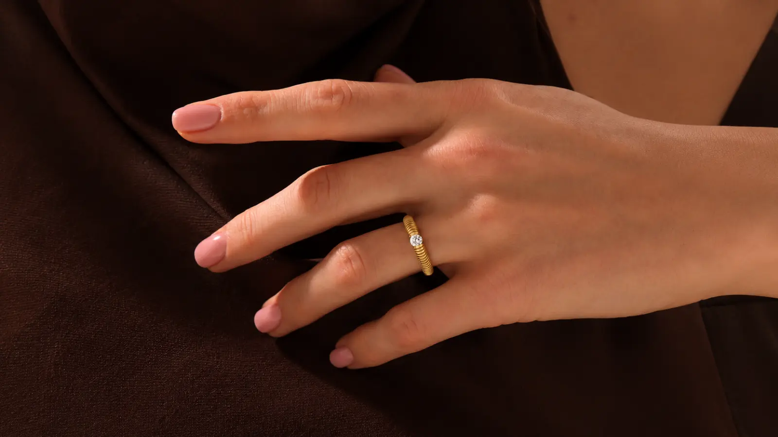 A hand wearing a minimalist modern yellow gold solitaire wedding ring with a slim textured band and delicate diamond accent Modern Wedding Rings