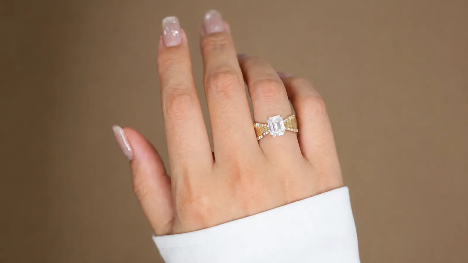 A hand wearing an emerald cut engagement ring with a twisted yellow gold pavé band and a modern sculptural design Unique Wedding Rings