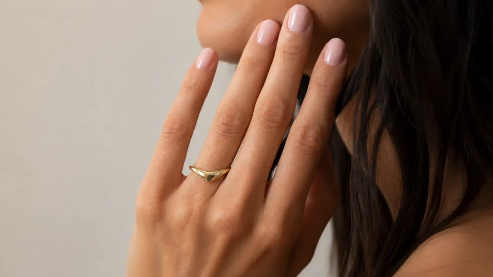 A hand wearing a modern yellow gold wave wedding ring with a smooth sculptural design and minimalist contemporary style
