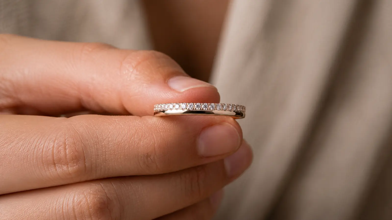 A moissanite half eternity wedding band is held between fingertips, highlighting its continuous row of sparkling stones and polished finish