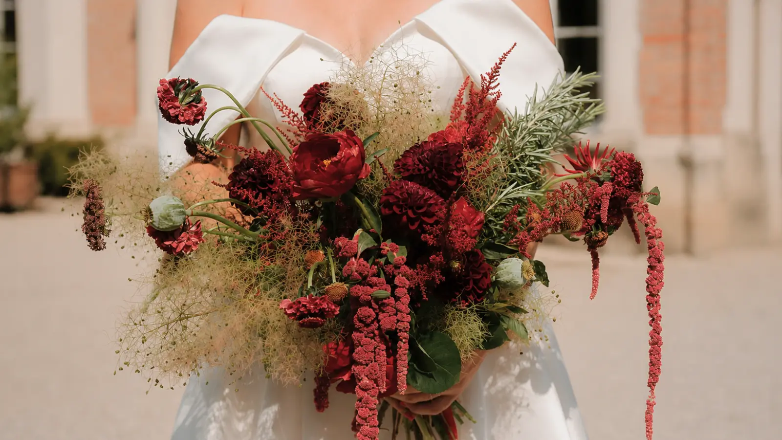 Bride holding a moody burgundy wedding bouquet with smoke bush, dark blooms and cascading amaranthus